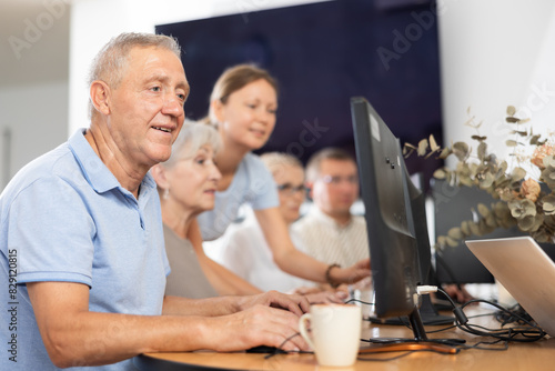 Elderly man learns how to work with computer in group at computer course