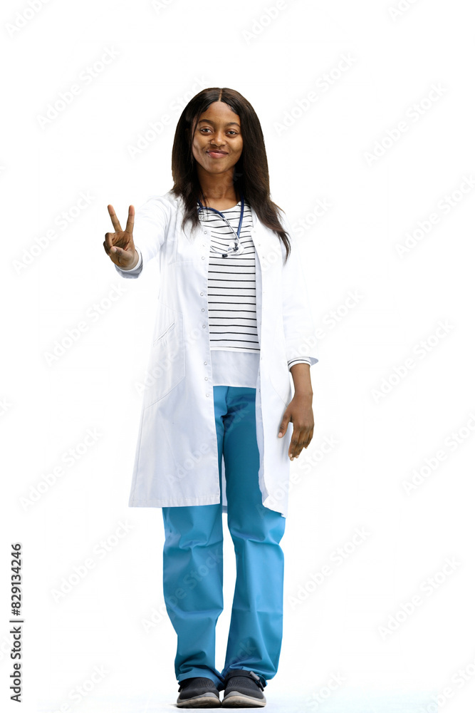 A female doctor, on a white background, in full height, shows a victory sign