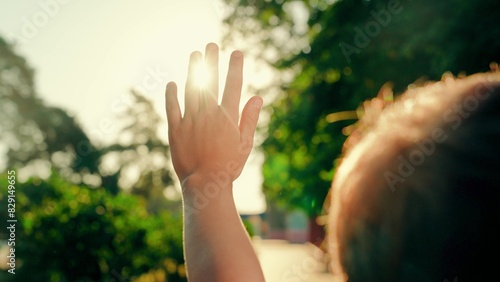 Child hand reaches out to sun, summer park. Kid dreams in park against sun. Child prayer, boy stretches out her hands to sun. Sunlight in hands of child, nature. Religion. Little girl playing outdoor