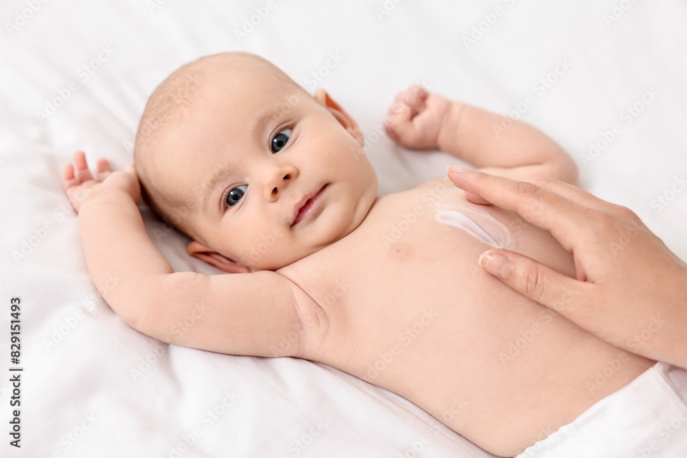 Woman applying body cream onto baby`s skin on bed, closeup Woman applying body cream onto baby`s skin on bed, closeup