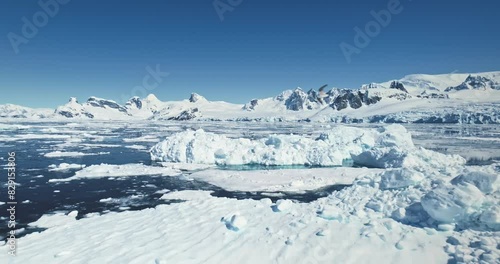 Fly over melting ice floes drifting polar ocean. Iceberg and towering snow coverd mountains in backdrop. Beauty of Antarctica landscape seascape. Ecology, climate change, global warming. Aerial shot