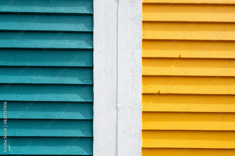 The join between two colorful and bright wooden exterior walls of pine clapboard. The walls are teal green and yellow with a white seam. The retro rough surface is textured siding boards painted bold. The join between two colorful and bright wooden exterior walls of pine clapboard. The walls are teal green and yellow with a white seam. The retro rough surface is textured siding boards painted bold.