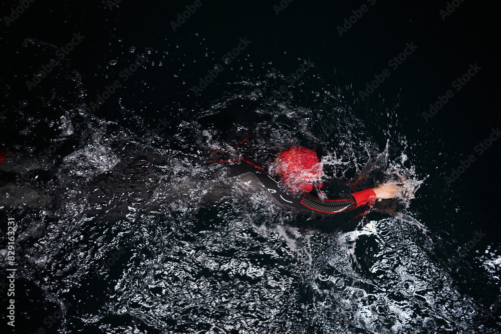 Fototapeta premium A determined professional triathlete undergoes rigorous night time training in cold waters, showcasing dedication and resilience in preparation for an upcoming triathlon swim competition
