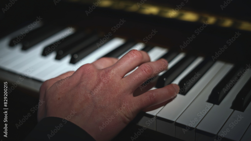 Fototapeta premium Close-up of hand playing piano. Media. Light falling on hand playing piano. Lonely hand is playing notes on piano
