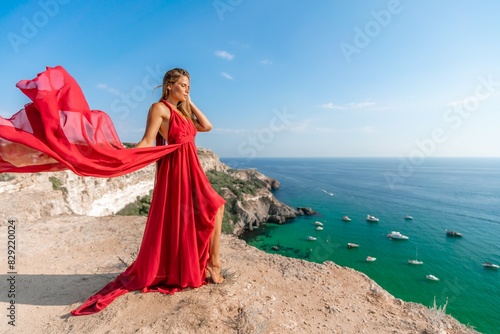 Woman sea red dress yachts. A beautiful woman in a red dress poses on a cliff overlooking the sea on a sunny day. Boats and yachts dot the background.