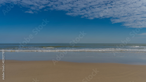 Serene minimalistic seascape. The waves of the turquoise ocean roll towards the shore  foaming and spreading over the sandy beach. Clouds in the blue sky. Copy space. Madagascar. Morondava. 