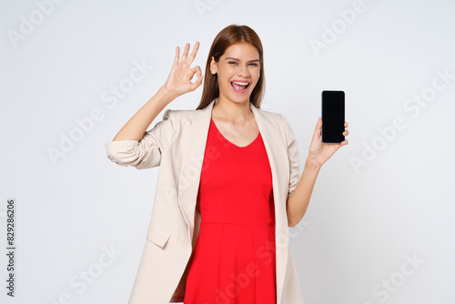 Asian woman, showing smartphone screen, app interface and ok sign, recommending application on mobile phone, standing over white background.