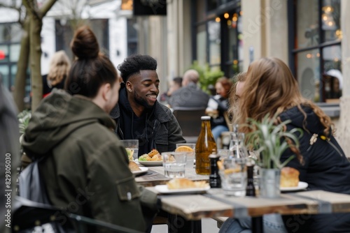 Group of friends having lunch in a street cafe. Cheerful african american man smiling and looking at his friend while sitting at the table