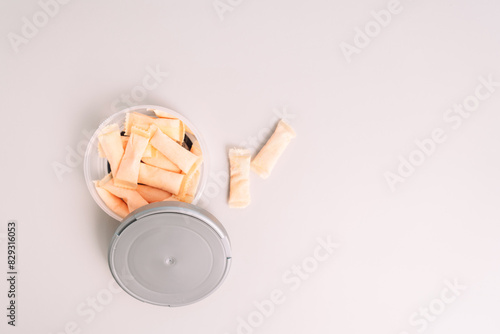 Plastic jar with fruit flavored snus sachets on a light background.