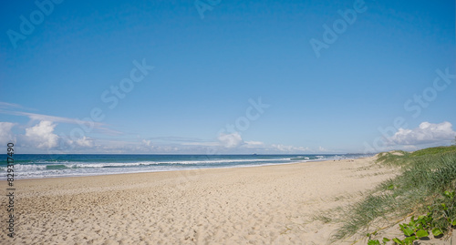A sunny day at the beach with sandy foreshore, crashing surf waves and blue sky at Kawana on the Sunshine Coast in Queensland Australia