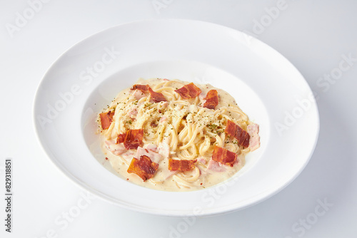 Spaghetti Carbonara topped with ham and bacon served in white plate isolated on white background. italian food.