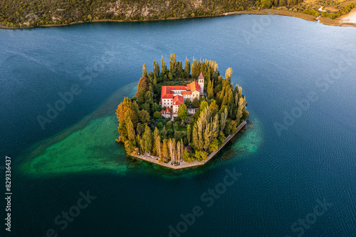 Visovac, Croatia - Aerial view of the amazing Visovac Christian monastery in Krka National Park on a bright summer morning with warm golden lights at sunrise and blue water