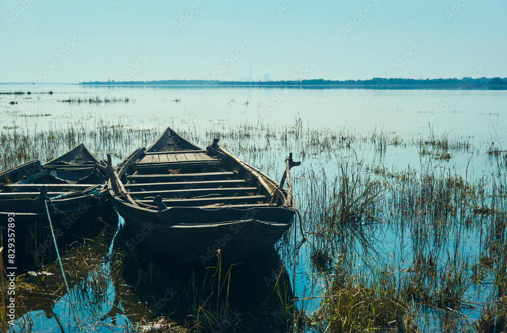 Fototapeta premium Pair of traditional wooden made fishing boats lying idly on grassland, submerged in shallow water of Damodar river embankment. Photo taken near Panchet Dam, in Purulia.