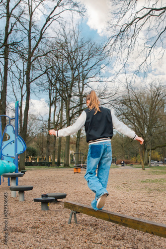 Teenage girl on a walking bar in a park with a simple swing for children. Vertical