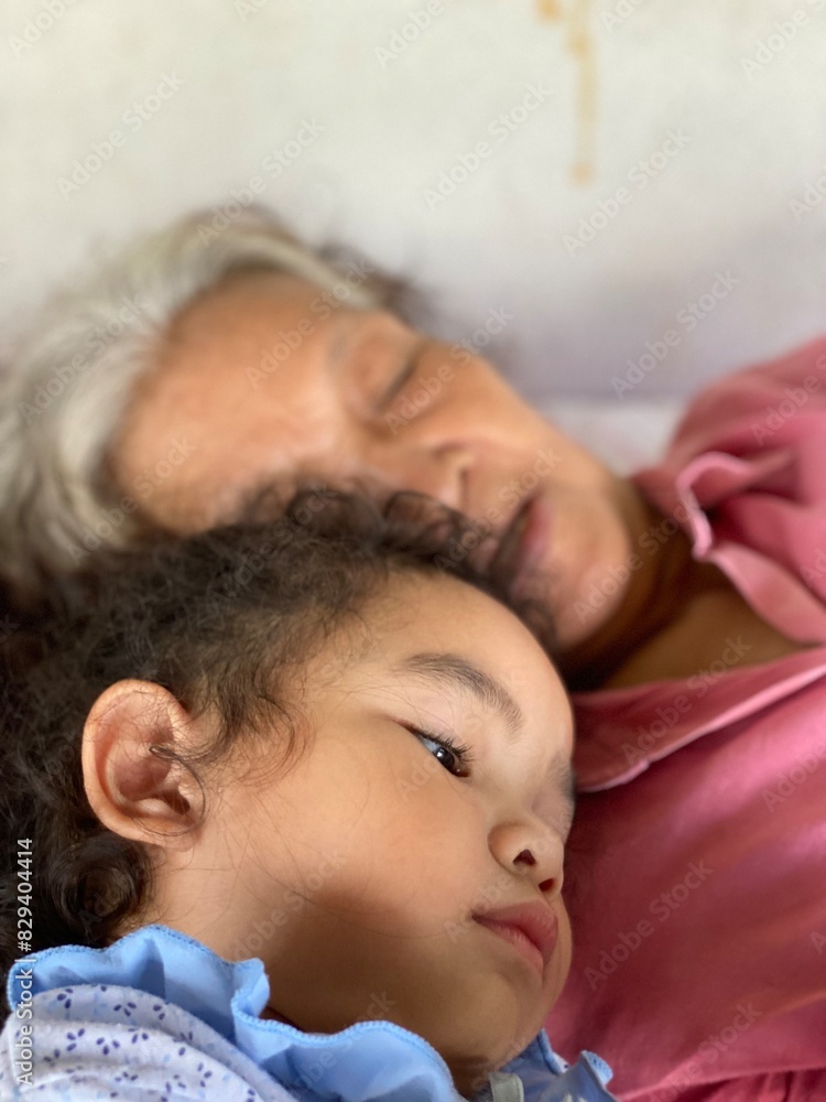 Asian senior woman with her little daughter lying on a sofa in her room Asian senior woman with her little daughter lying on a sofa in her room