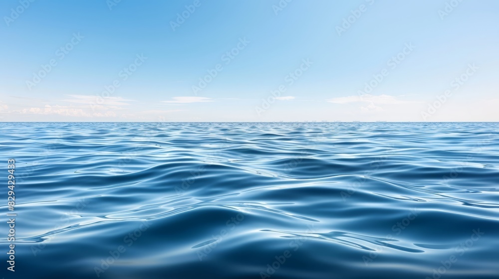 Fototapeta premium A vast expanse of blue water, topped with a clear sky bearing scattered clouds, descends into undulating waves below