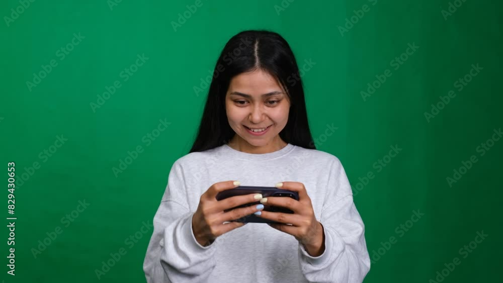 Studio shot. Young woman enjoys playing a mobile game on her smartphone, embracing digital entertainment and fun. Gaming in cyberspace using modern technology Studio shot. Young woman enjoys playing a mobile game on her smartphone, embracing digital entertainment and fun. Gaming in cyberspace using modern technology