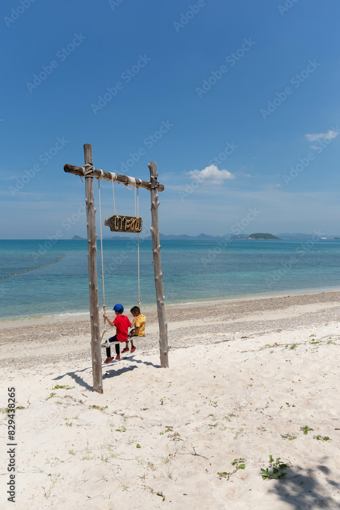 Two little children sitting on a swing on the beach Two little children sitting on a swing on the beach