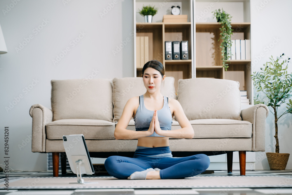 Asian Woman Doing Yoga and Watching Online Tutorials on Laptop, Training in Living Room at home Asian Woman Doing Yoga and Watching Online Tutorials on Laptop, Training in Living Room at home