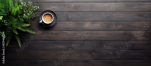The top down view of a black wooden office desk features a computer keyboard notepad plant and cup of coffee There is ample space for additional content in the image