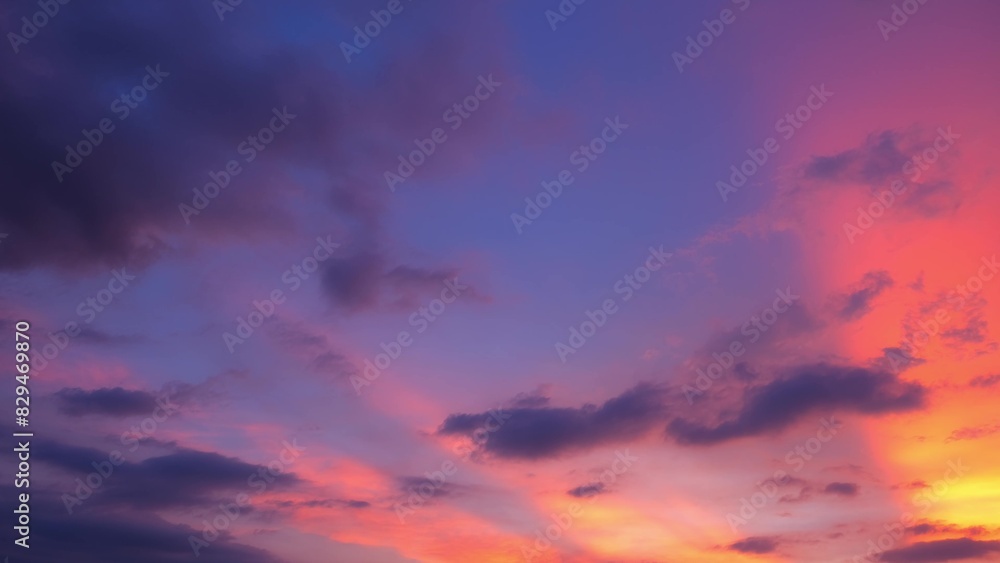 A stunning sunset sky with a gradient of colors transitioning from deep blue to vibrant pink and orange hues. Dark clouds are scattered across the sky. Sunset sky background.
