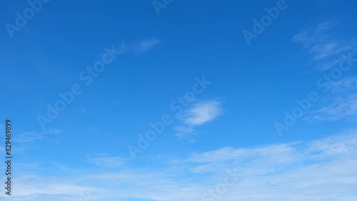 A clear blue sky with a few scattered white clouds. The sky transitions from a deeper blue at the top to a lighter blue near the horizon, creating a calm and peaceful atmosphere. Cloud background. 