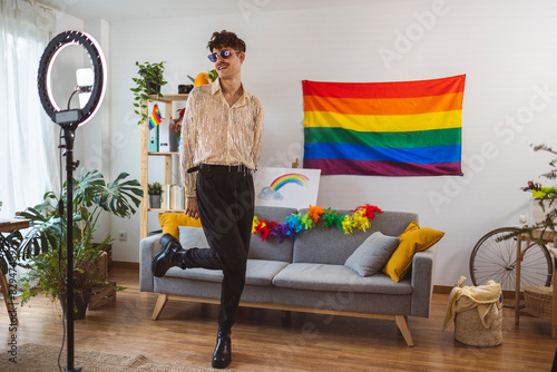 Smiling influencer vlogging with mobile phone in front of rainbow flag at home photo