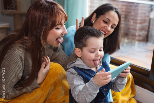 Happy boy sticking out tongue and taking selfie with family through smart phone at home photo