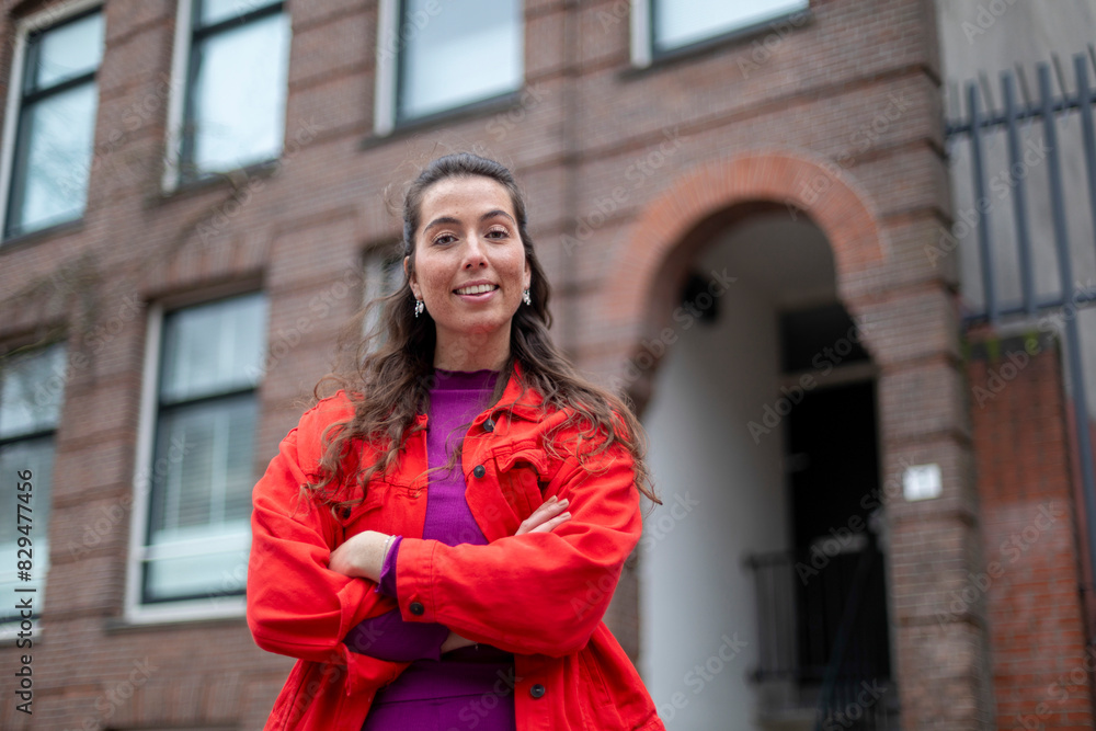 Smiling woman with arms crossed standing in front of building Smiling woman with arms crossed standing in front of building
