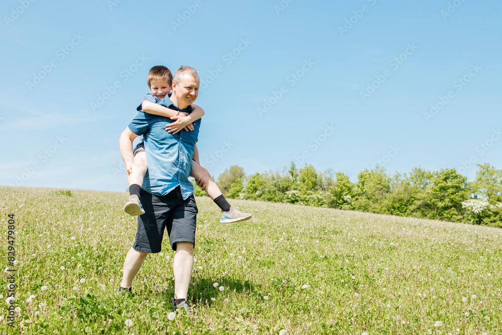 Father giving piggyback ride to son on dandelion field Father giving piggyback ride to son on dandelion field