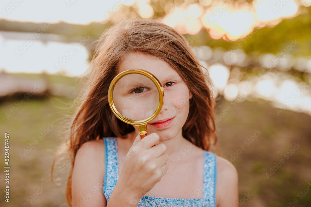 Redhead girl looking through with magnifying glass at garden Redhead girl looking through with magnifying glass at garden