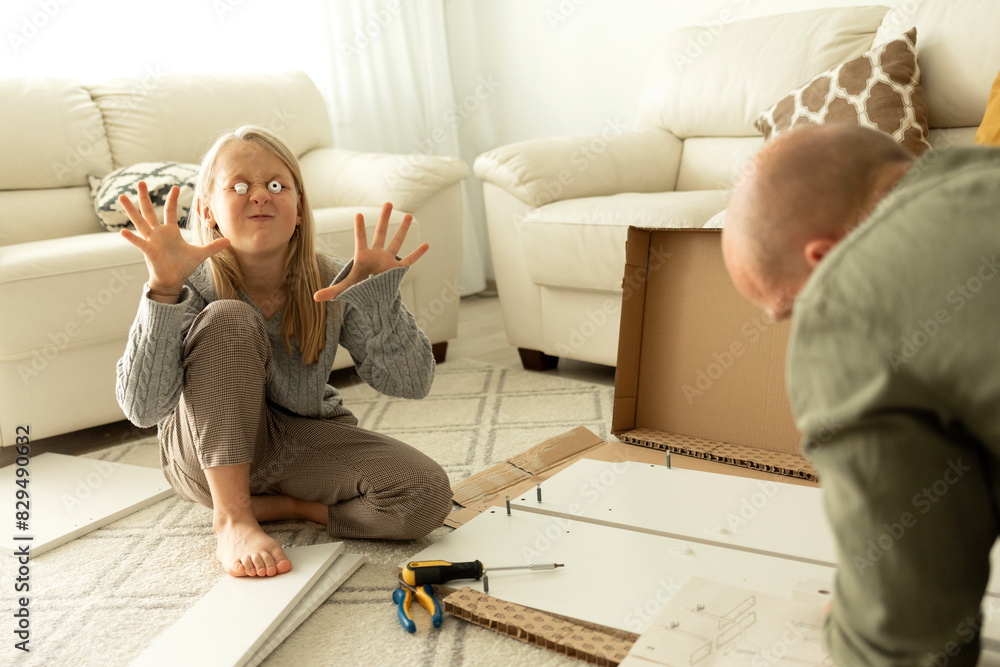 Girl with spooky eyes gesturing near father assembling furniture at home Girl with spooky eyes gesturing near father assembling furniture at home