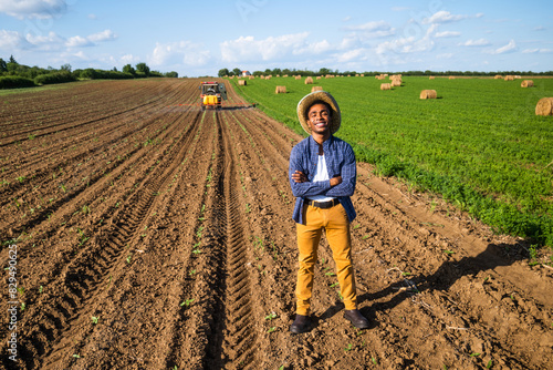 African farmer is standing in his agricultural field. He is supervising the spraying of the field.