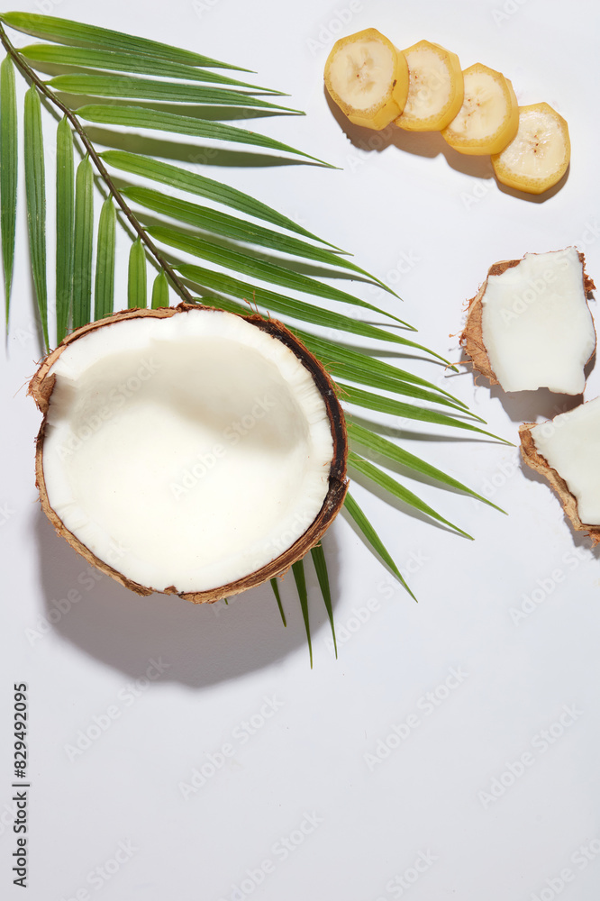 Top view photography at the white flat with banana and coconut flat lay above, banana slices arranged in a row next to some dried coconut pieces and a branch of coconut leaves decorated, blank space Top view photography at the white flat with banana and coconut flat lay above, banana slices arranged in a row next to some dried coconut pieces and a branch of coconut leaves decorated, blank space