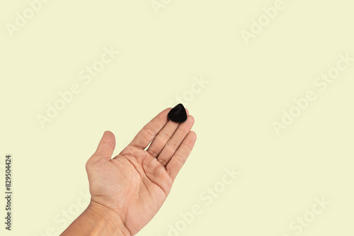 Black male hand holding a guitar pick isolated on light green background