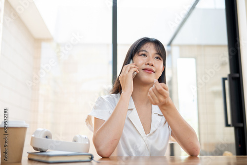 Free Download A charming Asian woman is talking on the phone with someone while sitting at a table in a cafe. - GFXLoad