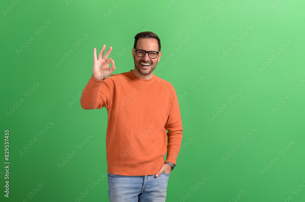 Portrait of confident salesman with hand in pocket showing OK sign while posing on green background Portrait of confident salesman with hand in pocket showing OK sign while posing on green background