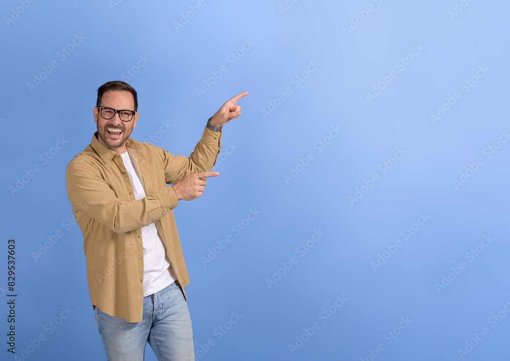 Portrait of young happy salesman aiming at copy space for marketing new product on blue background Portrait of young happy salesman aiming at copy space for marketing new product on blue background