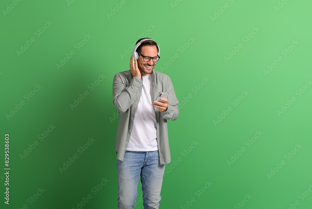 Smiling young man using mobile phone and answering calls over headphones on green background Smiling young man using mobile phone and answering calls over headphones on green background