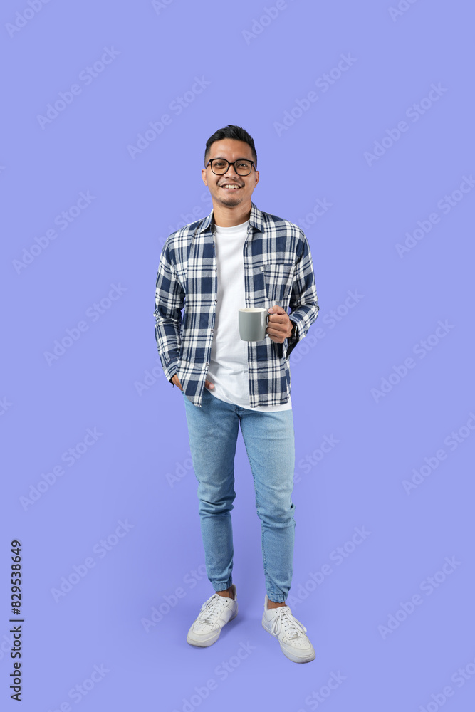 Full-length Portrait of a young Asian man smiling while holding a cup standing isolated over a purple background Full-length Portrait of a young Asian man smiling while holding a cup standing isolated over a purple background