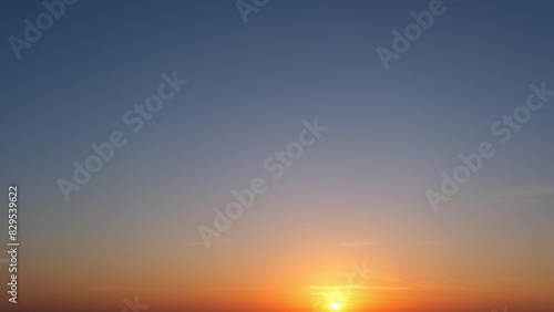 A serene sunrise with the sun just above the horizon  casting a warm golden glow. The sky transitions from deep blue at the top to orange near the horizon  creating a tranquil gradient. 