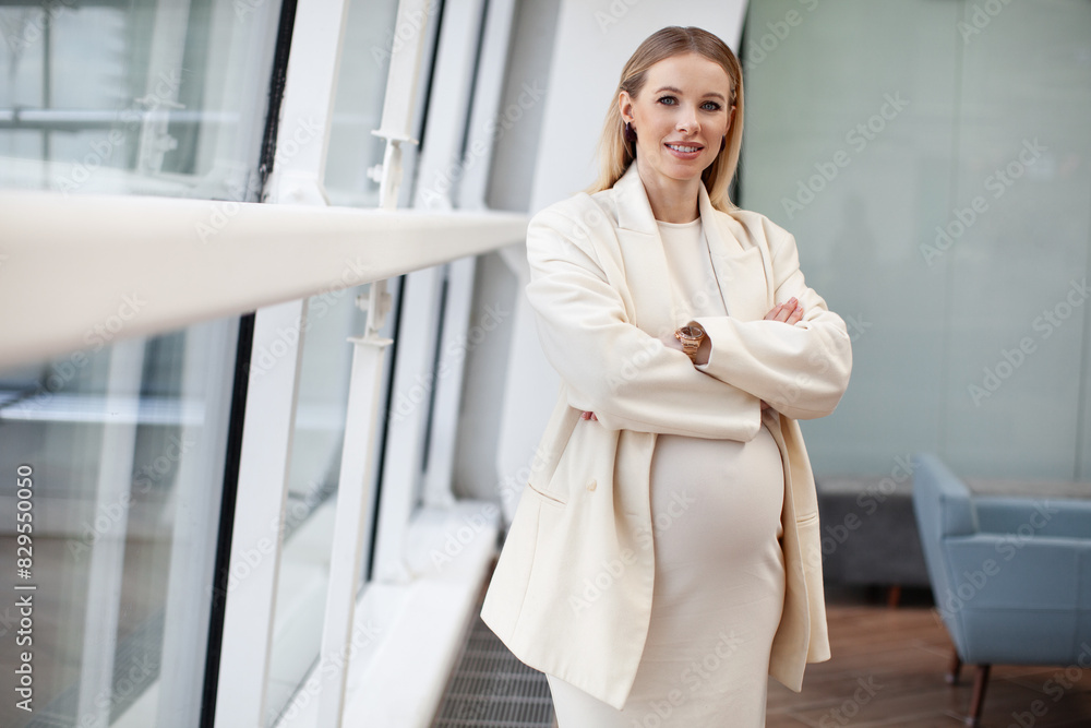 Beautiful, confident pregnant blonde woman in stylish and fashionable clothing a white dress and blazer looking at the camera in a corporate office setting