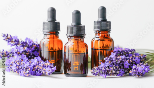 A trio of aromatic essential oil bottles are placed alongside purple flowers on a surface