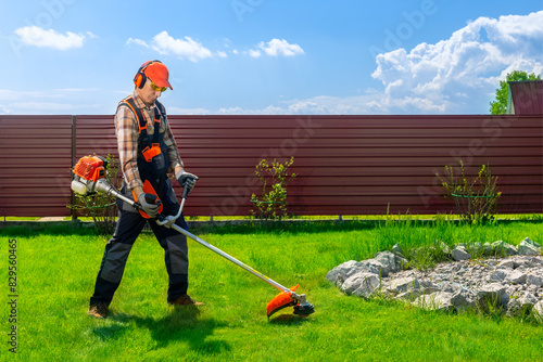 Quadro su tela Worker, man mowing tall grass with petrol lawn trimmer in the backyard of house