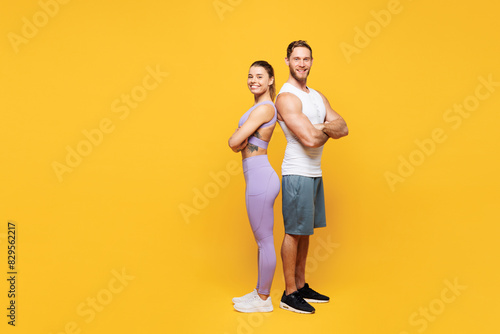 Full body young cool strong fitness trainer sporty two man woman wear blue clothes spend time in home gym stand back to back look camera isolated on plain yellow background. Workout sport fit concept.