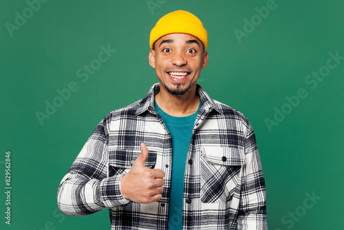 Young smiling happy cheerful man of African American ethnicity he wear shirt blue t-shirt yellow hat showing thumb up like gesture isolated on plain green background studio portrait Lifestyle concept