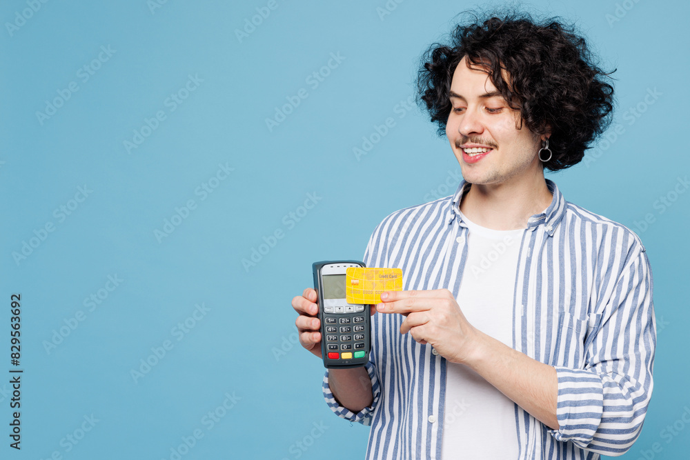 Young man he wear shirt white t-shirt casual clothes hold wireless modern bank payment terminal to process acquire credit card isolated on plain pastel light blue cyan background. Lifestyle concept.