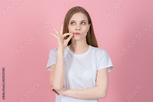 Attractive caucasian young blonde woman in casual white t-shirt showing zip gesture isolated on pink studio background. Trust, Silence, Mystery, Secret, Confidential.