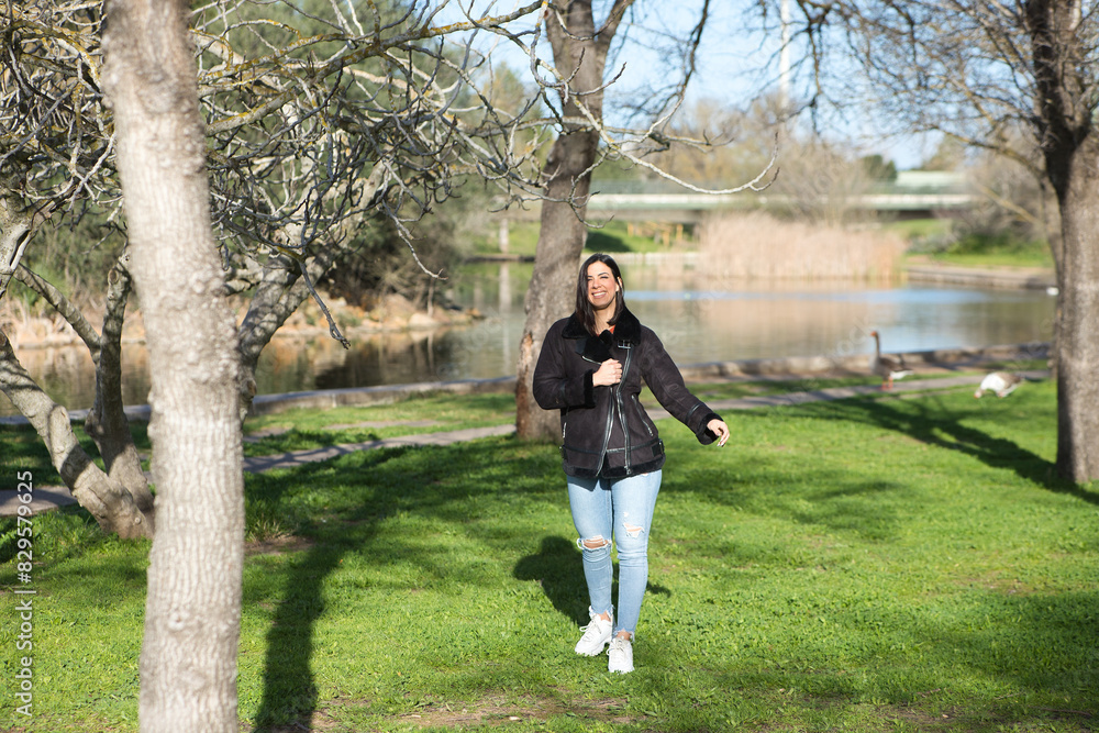 Young and beautiful brunette woman with short hair and jeans and black jacket, walks through the park among the leafless trees on a cold day, the woman makes different body postures. Young and beautiful brunette woman with short hair and jeans and black jacket, walks through the park among the leafless trees on a cold day, the woman makes different body postures.