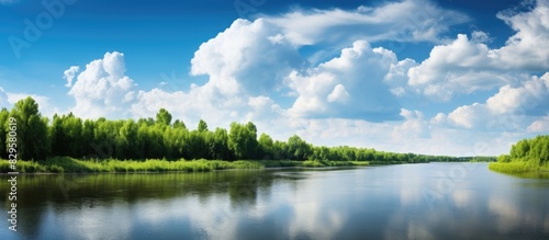 A scenic summer view featuring a river lush forest and verdant riverbanks set against a sunny sky with fluffy white clouds ideal for a copy space image